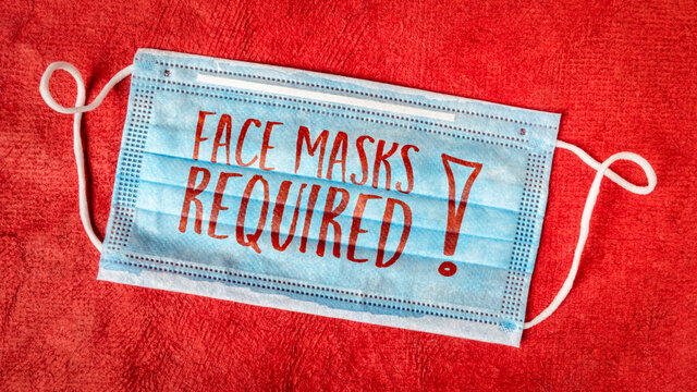 face masks required - text on a disposable mask against red textured paper, business sign during the coronavirus covid-19 pandemic and social distancing