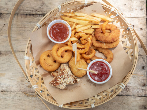 Baskets of Onion Rings, Curly Fries, french fries, and chicken nugget on wooden table.