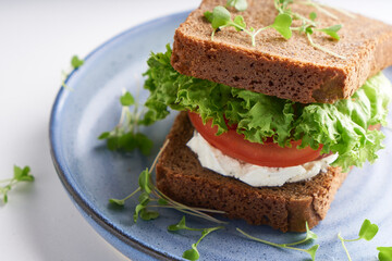 healthy sandwich with gluten-free bread, tomato, lettuce and germinated microgreens served in plate on white table