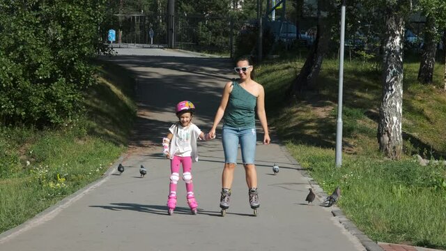 Happy Young Mother and her Cute Little Daughter Inline Skating Together in a City Park. Childhood, Summer Activities and Mothers Day Concept