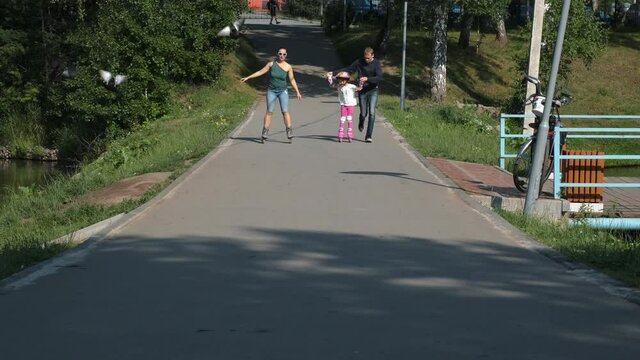 Family of Three Roller Skating in a Summer Park. Little Girl with Mom and Dad Enjoying Time Together. Slow Motion. Happy Childhood, Summer Family Activities and Healthy Lifestyle Concept