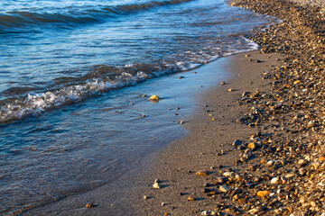 Douces vagues s'échouant sur la rive en bord de lac, sur la plage de sable et de cailloux
