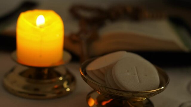 Communion hosts in twilight illuminated by the light of a lit candle rosary