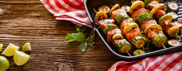 Skewers of salmon with zucchini in a grill pan on a wooden background with copy space