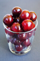 red juicy cherry in a clear glass glass on a dark gray background side view . ripe summer berries