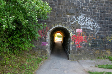 Plakat Eine Unterführung, Tunnel für Fußgänger und Fahrradfahrer.Die Bruchsteinmauer ist mit Graffiti bemalt.