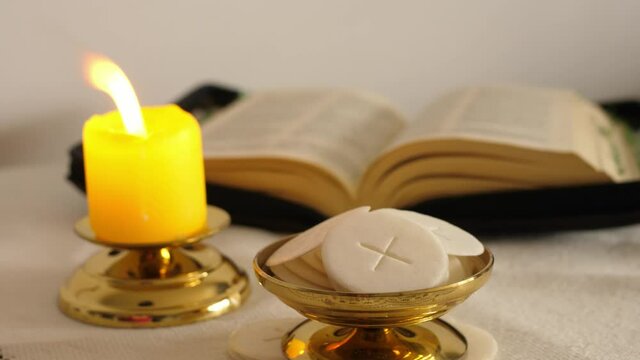 communion hosts lit candle and holy bible 