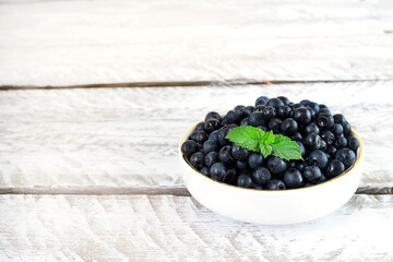 Fototapeta na wymiar Ripe juicy blueberries in a white bowl stands on a vintage white wooden table. The bowl is decorated with fresh mint leaves. Delicious and healthy summer berries, healthy food, vitamin dessert