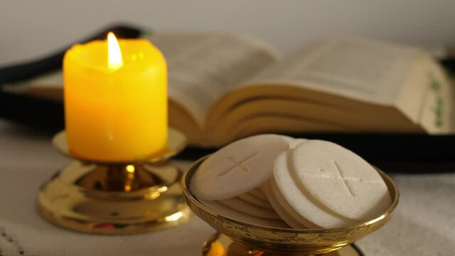 communion hosts lit candle and holy bible 