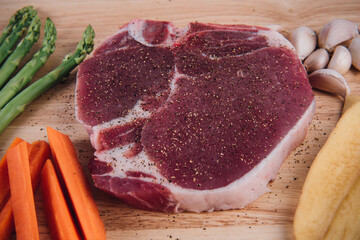 Raw meat t-bone steak with herbs, spices, potato, carrot, garlic and asparagus on a wood background