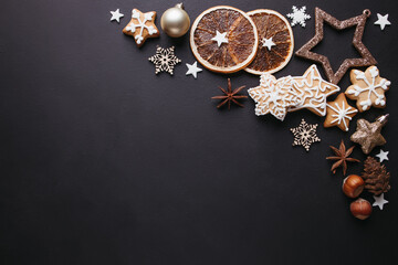 Winter holiday vibes. Frame made of festive decorations, dried oranges, spices and gingerbread on black background. Seasonal background, Christmas, New Year composition. Flat lay, copy space