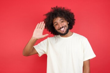 Fototapeta na wymiar Portrait of cheerful, outgoing friendly-looking young man wearing casual clothes raise one hand and wave, saying hi or hello and smiling with carefree expression as make goodbye or welcome gesture.