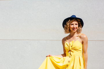 Fototapeta premium Portrait of a smiling young woman with summer hat and trendy yellow dress standing outside
