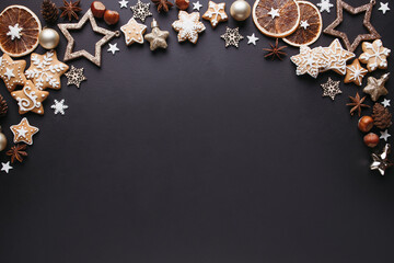 Winter holiday vibes. Frame made of festive decorations, dried oranges, spices and gingerbread on black background. Seasonal background, Christmas, New Year composition. Flat lay, copy space