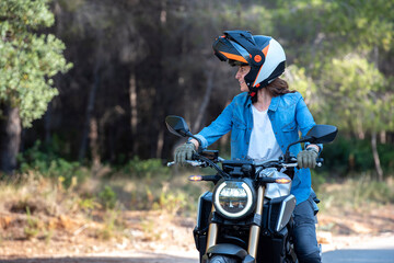 Young girl with brown hair, on a large motorbike, with a helmet on.