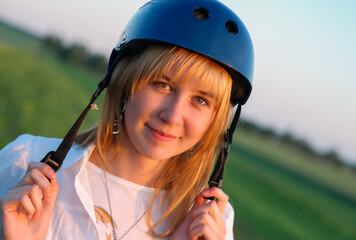 Young beautiful girl in a protective sports helmet outdoors in the evening at sunset
