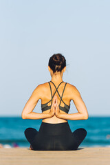 young woman from the back doing yoga in front of the sea on a sunny day