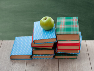 Back to school, pile of books in colorful covers and green apple on wooden table with empty green school board background. Distance home education. Quarantine concept of stay home.
