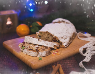 Traditional homemade Christmas stollen cake with raising, berries and nuts, covered with powdered sugar on decorated table with orange fruits and cinnamon. Concept of celebration of festive holidays.