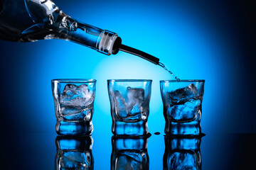 Vodka is poured from bottle into glasses with ice.
