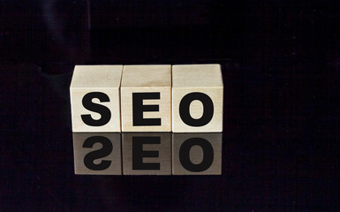 SEO text on wooden cubes on black glass background.