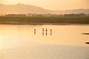 Obraz na płótnie Canvas Femmes marchant dans un fleuve au coucher de soleil