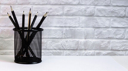 Black pencils stand in a black glass against the background of a light brick wall. For business.