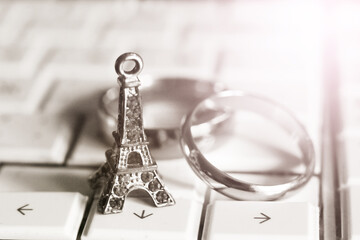 A statue of the Eiffel Tower and wedding rings on the laptop keyboard, black and white.