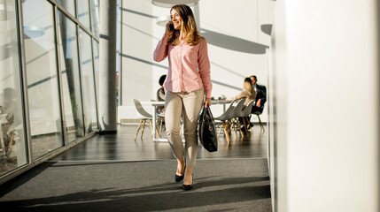 Naklejka premium Businesswoman on cell phone walking in the office
