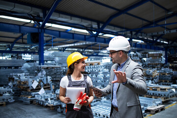 Manager wearing hardhat and industrial worker discussing about production in metal factory....