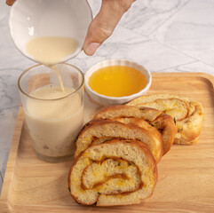 The yellow bread is placed on a wooden tray and has tofu in a glass placed on a marble table.