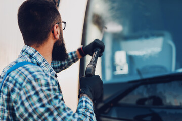 Young man washing bus using high pressure water. Selective focus.