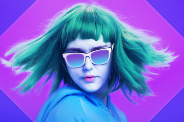Art collage with alternative funky girl with blue hair on a bright blue purple background. Close up fashion portrait young beautiful woman in hoodie and glasses. Unusual youth fashion concept.
