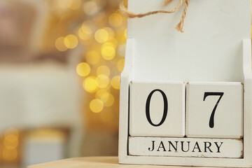 White wooden calendar with cubes and date January 07 and lights bokeh from a garland in the background. Orthodox Christmas date. Copy space..