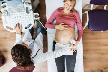 Beautiful and happy expectant mother at gynecological examination with ultrasound medical equipment.