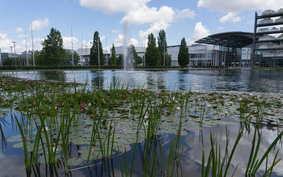 Munich, Bavaria / Germany - July 12, 2020: buildings with logos of the „Messe München“ (trade fair) and "ICM - International Congress Center Munich", in the fore a park with a pond with waterlily