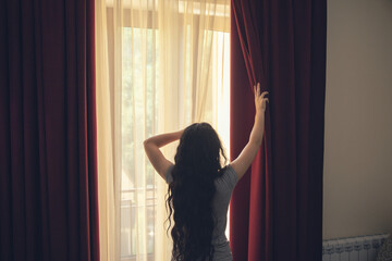 Fototapeta na wymiar happy woman stretches and opens the curtains at window