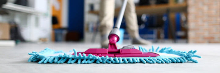 Male hand hold blue plastic mop against modern cabinet closeup background. Business office cleaning concept