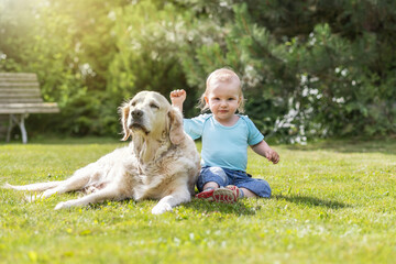 Cute liitle baby boy is waving at the camera posing with Golden Retriever dog in the garden