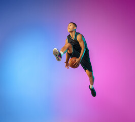 Fototapeta na wymiar Winner. Young basketball player in action, motion in high jump on gradient background in neon. Concept of sport, movement, energy and dynamic, healthy lifestyle. Training, practicing, trendy colors.