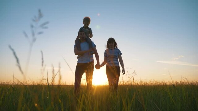 Happy family in the park at sunset. Mom, dad and baby are happily walking in the fresh air. Father holds son on shoulders. The boy makes a helpless gesture, plays simulates an airplane.