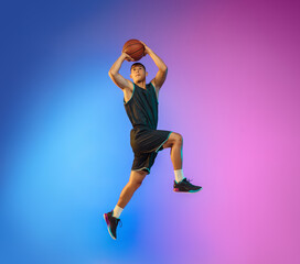 Winner. Young basketball player in action, motion in high jump on gradient background in neon. Concept of sport, movement, energy and dynamic, healthy lifestyle. Training, practicing, trendy colors.