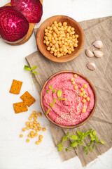 Hummus with beet and microgreen basil sprouts in wooden bowl on a white wooden background. Top view, close up.
