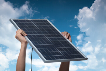 Hand holding a solar panel on blue sky background,alternative clean green energy concept