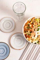 Ensalada Caesar con mucho pollo, salsa crotones de pan y maiz en un bowl blanco sobre un mantel de rayas con otros platos de ceramica en azules y beige para acompañantes.