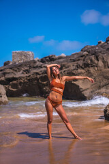 Lifestyle, Caucasian with a luxurious brown swimsuit enjoying the summer next to sea rocks. Out of the water stretching