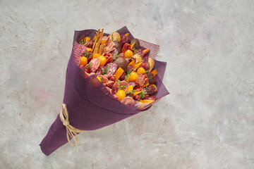 Tasty edible bouquet consisting of sausages, cheese and tomatoes on a light background.