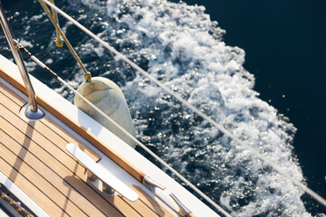 View of the teak deck of a sailing yacht moving on a calm surface of the sea.