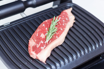 A piece of fresh meat with coarse salt and a sprig of rosemary. Juicy beef steak on the electric grill. - 368850264