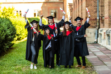 Five graduates posing in front of the university